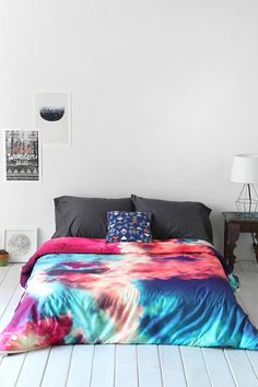 a bed covered in a colorful comforter next to a night stand with two lamps