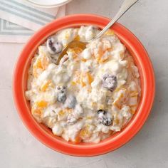 an orange bowl filled with fruit salad on top of a white table next to a fork