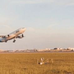 an airplane is taking off from the runway in front of a field with grass and buildings