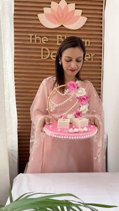 a woman holding a pink cake in front of a sign that says the flower decor