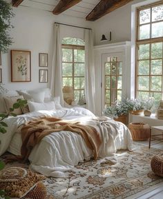 a bedroom with lots of windows and blankets on the bed, along with plants in baskets