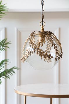 a clear glass ball hanging from a brass chandelier over a white table with a potted plant in the background