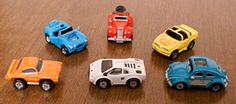 six toy cars sitting on top of a wooden table next to an orange and blue car