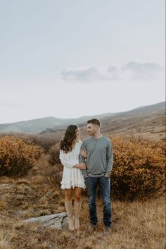 an engaged couple standing in the middle of a field