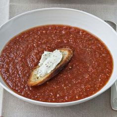 a white bowl filled with soup and bread on top of a gray table cloth next to silverware