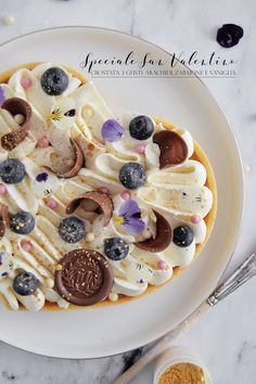 a white plate topped with a dessert covered in cream and blueberries on top of a table