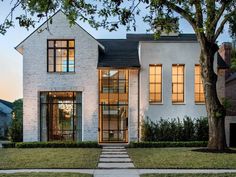 a white brick house with large windows and steps leading up to the front door at dusk