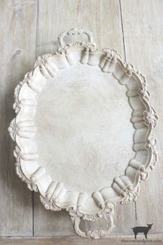 an old white plate sitting on top of a wooden floor next to a black cat