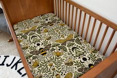 a wooden crib with a patterned sheet in the middle and a rug on the floor next to it