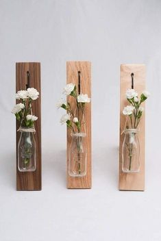 three vases with flowers in them are hanging on wood