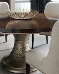 a dining room table with chairs and a bowl on it's centerpiece, in front of a window