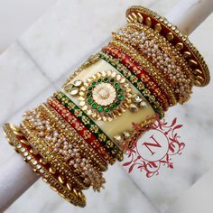 Indian Bollywood Style Bridal Red & Green Chuda Set. Beautified With Pearls Bunches Bangles. Center Piece Is Prettified With High Quality Glass Kundan In Gold & Green Color On Cream Acrylic Base. Floral Shape Metal Figure In Center Of Kundan Fitting Is Making This Ensemble More Adorable. Kundan Work Kada At Both End Of This Chuda Is Making It Perfect For Your Special Day. Be An Angel And Create A Splendid Impact On Everyone By Wearing This Gorgeous Design. This is a set of 26 Bangles (13 Wedding And Navratri Stone Work Sets, Red Stone Work Wedding Lehenga, Bollywood Bridal Accessories For Marriage, Red Lehenga With Stone Work For Wedding, Red Wedding Lehenga With Stone Work, Festive Bridal Accessories With Tilla For Marriage, Festive Kundan Lehenga For Marriage, Temple Jewelry Sets With Gota Work For Wedding, Red Tilla Bridal Sets For Marriage