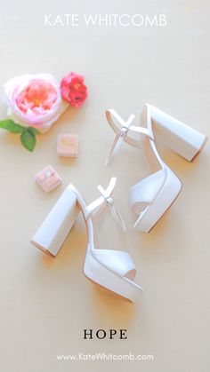 white high heeled shoes sitting on top of a table next to a flower and blocks