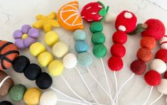 several different types of felt balls and fruit on a white plate with toothpicks