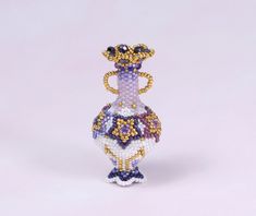 a beaded figurine is displayed on a white surface with purple and yellow accents