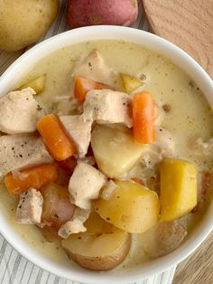 a white bowl filled with chicken and potatoes on top of a wooden table next to a spoon