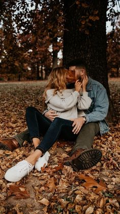 a man and woman sitting under a tree in the leaves with their faces close to each other