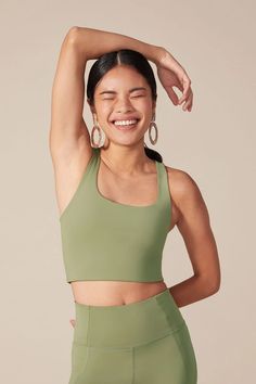 a woman wearing a green sports bra top and matching leggings with her hands on her head