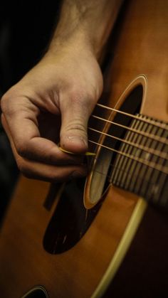 a close up of a person playing an acoustic guitar with their hand on the strings