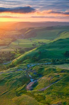 the sun is setting over green hills and valleys with small streams running through them,