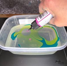 a person is painting in a container with green and blue paint on the inside of it