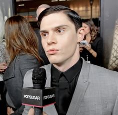 a man in a suit holding a microphone and talking to the camera at an event