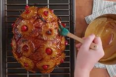 a person holding a spatula over a cooked ham on a grill with pineapples