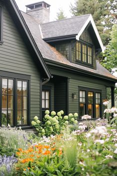 a green house with lots of flowers in the front yard and windows on each side