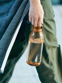 a person holding a glass bottle with water in it's sleeve and wearing green pants