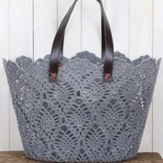 a gray crocheted bag sitting on top of a wooden table next to a white wall