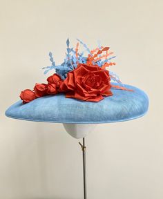 "A stunning pale blue and orange wide brim hatinator.  This gorgeous statement headpiece is made using sinamay straw in a beautiful shade of powder blue. Central to this hat, is a  large handmade silk dupion rose in burnt orange and five matching rose buds that cascade down the brim to one side.  A small collection of powder blue and orange feathers float out  from the top of the rose, adding movement and drama to the overall finished hat.  This particular design has a shallow brim and is secured with a double metal headband that it ribbon wrapped in a colour to blend in with your own hair colour. This band is completely invisible when the hat is on.  Measuring 44cm side to side and 37cm front to back. It is made to a standard 22\" diameter, however, if you require a smaller fit I can prov Blue Summer Fascinator Hat, Blue Fascinator With Handmade Flowers For Kentucky Derby, Blue Handmade Flowers Fascinator For Races, Blue Mini Hats With Handmade Flowers For Royal Ascot, Light Blue Summer Hats For Races, Light Blue Summer Hat For Races, Blue Fascinator For Royal Ascot Garden Party, Blue Fascinator For Garden Party And Royal Ascot, Blue Fascinator For Garden Party At Royal Ascot