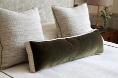 two pillows on top of a bed next to a night stand with a lamp in the background