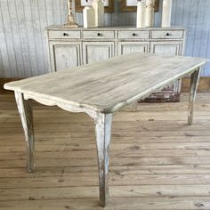 an old white table in a room with wooden floors and dressers behind the table