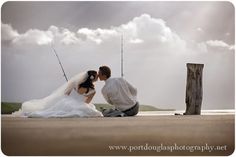 a bride and groom are sitting on the beach with fishing rods in their hands as they kiss