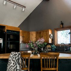 a kitchen with black appliances and wooden chairs next to a counter top area that has flowers in a vase on it