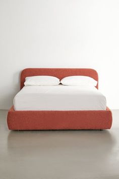 a bed with two pillows on top of it and an orange headboard in the middle