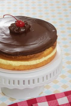 a cake with chocolate frosting and a cherry on top sitting on a white plate