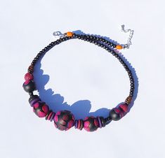 a black and pink beaded necklace on a white surface with an orange ball hanging from it's end