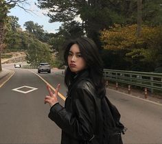 a woman standing on the side of a road holding her hand up in the air