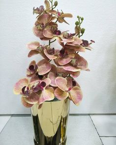 a gold vase filled with pink flowers on top of a white tile floor next to a wall