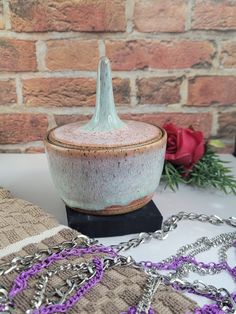 a ceramic container sitting on top of a table next to a chain link bracelet and red rose