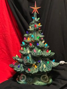 a green ceramic christmas tree with lights on it's base and a red curtain in the background