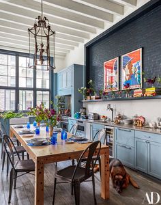 a kitchen with blue cabinets and wooden table surrounded by chairs in front of a dog laying on the floor