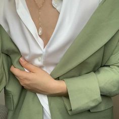 a woman wearing a green blazer and white shirt with her hands on her chest