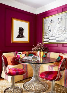 a dining room with red walls and chairs around a glass table that has colorful cushions on it