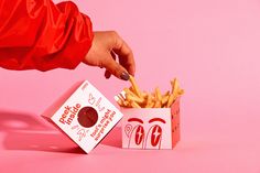 a hand reaching for french fries in a box on a pink background with the lid open