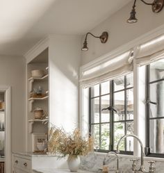 a kitchen with white cabinets and marble counter tops, two large windows over the sink