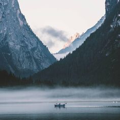 a boat floating on top of a lake surrounded by mountains and fog in the air