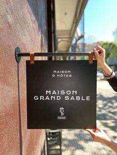 a woman holding up a sign that says maison grand sable on the side of a building