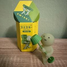 a small toy holding a green umbrella next to a box